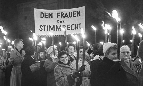 Frauen demonstrieren bei Dunkelheit mit Fackeln und Transparenten für das Frauenstimmrecht.