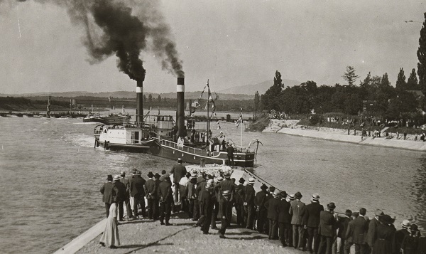 Schwarz-Weiss-Foto. Das erste Schiff fährt mit grosser Rauchwolke in den neuen Hafen in Basel ein.