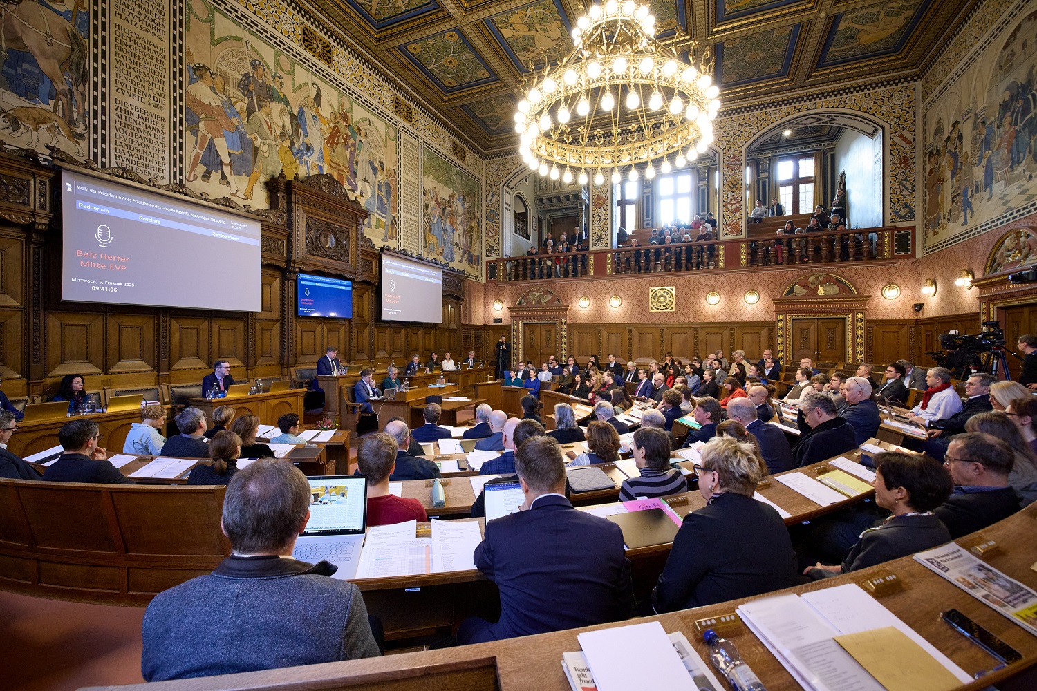 Vollbesetzter Grossratssaal, vorne wird auf zwei Leinwänden Thema und Redner angezeigt.