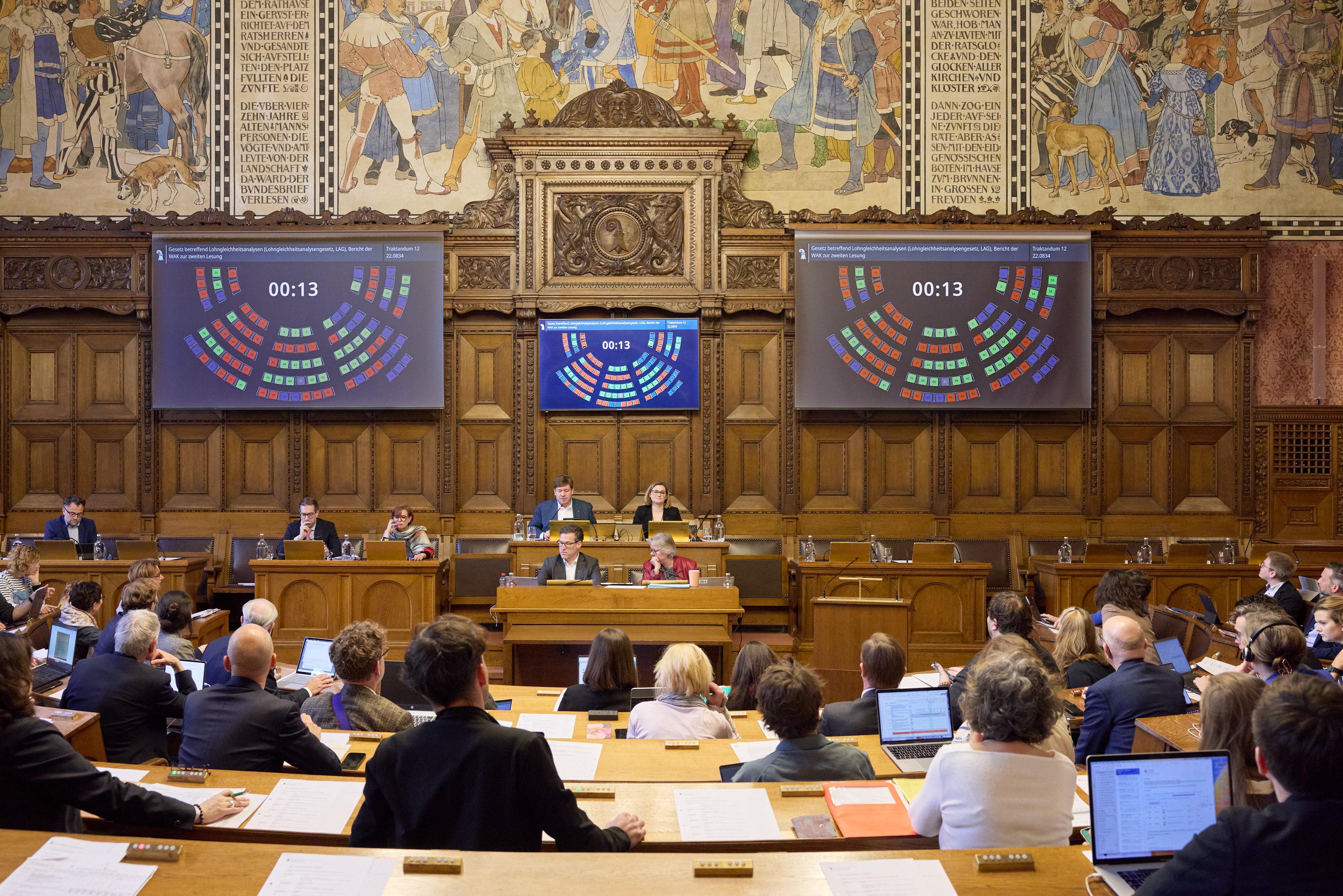 Vollbesetzter Grossratssaal, vorne wird auf zwei Leinwänden Thema und Redner angezeigt.