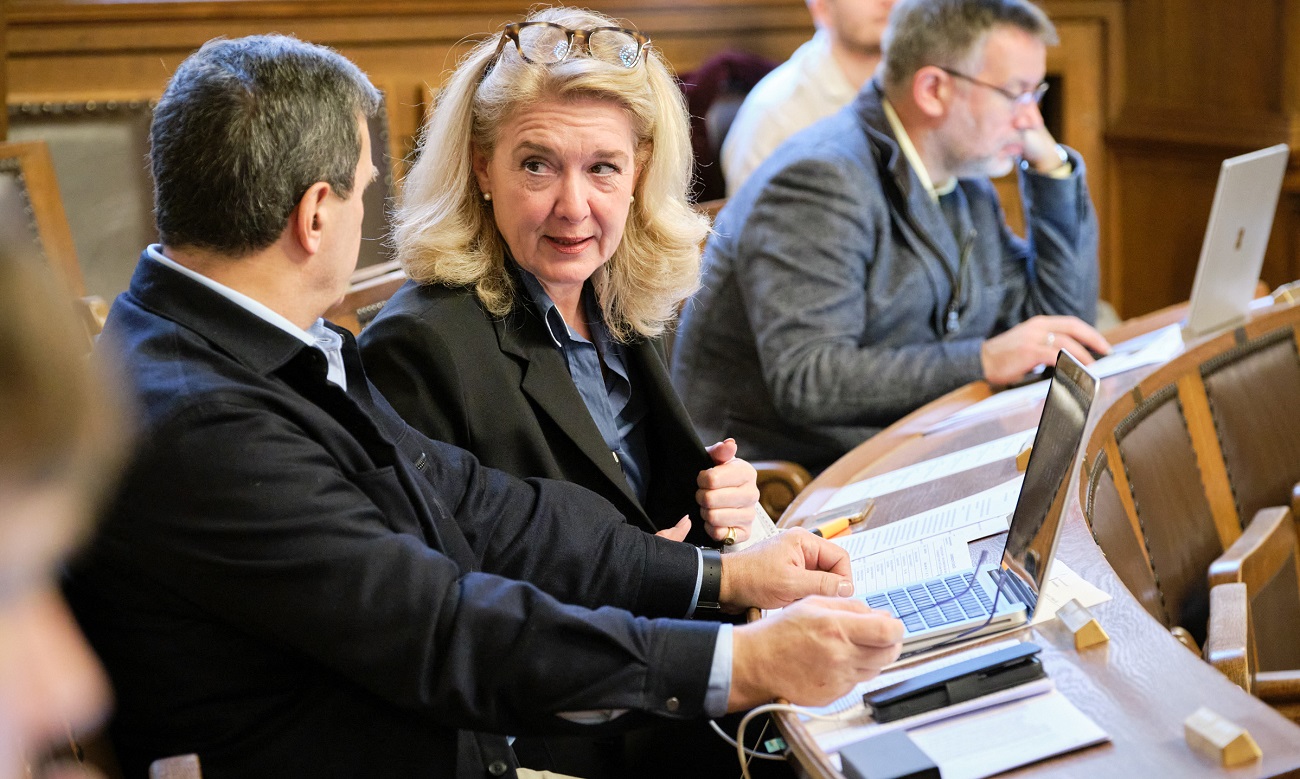 Drei Grossratsmitglieder auf ihren Sitzen, diskutierend bzw. in Arbeit vertieft.